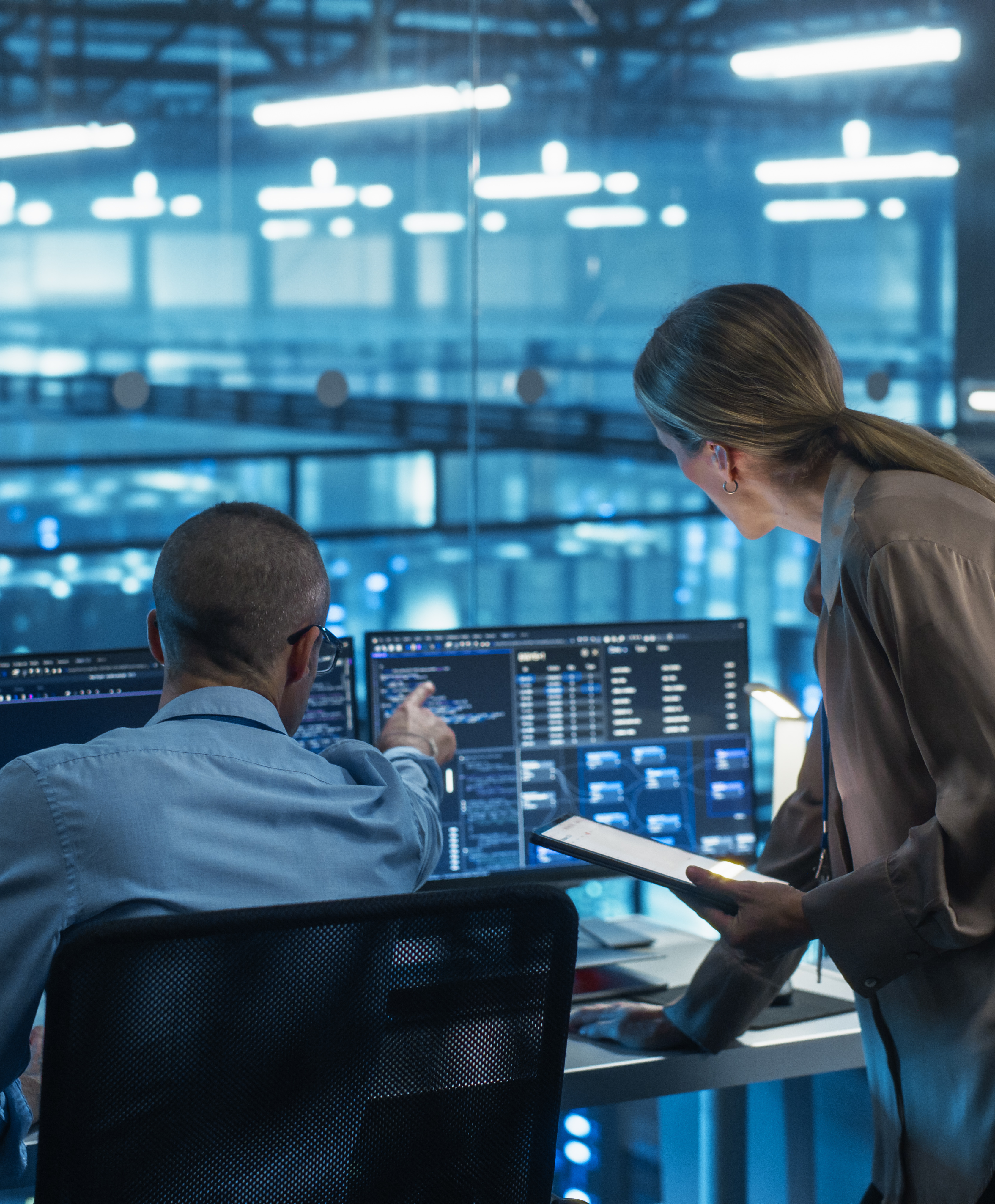 Two engineers reviewing data on multiple monitors in a high-tech facility