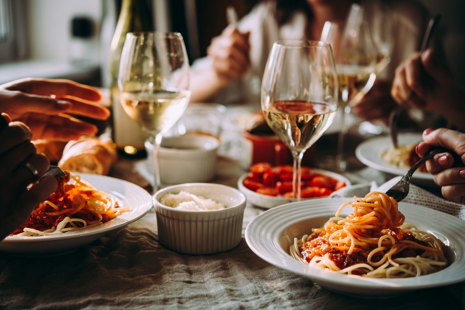 Diners sharing spaghetti and white wine at an Italian dinner table